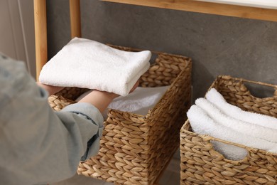 Woman putting towel into storage basket indoors, closeup