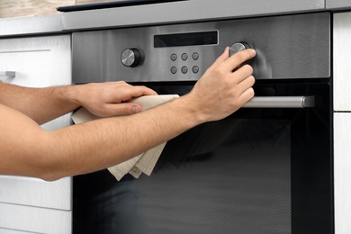 Photo of Young man adjusting oven settings in kitchen, closeup
