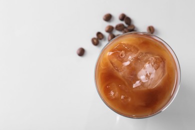 Glass of iced coffee and beans on white table, top view. Space for text