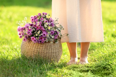 Photo of Woman with wicker basket of beautiful wild flowers outdoors, closeup