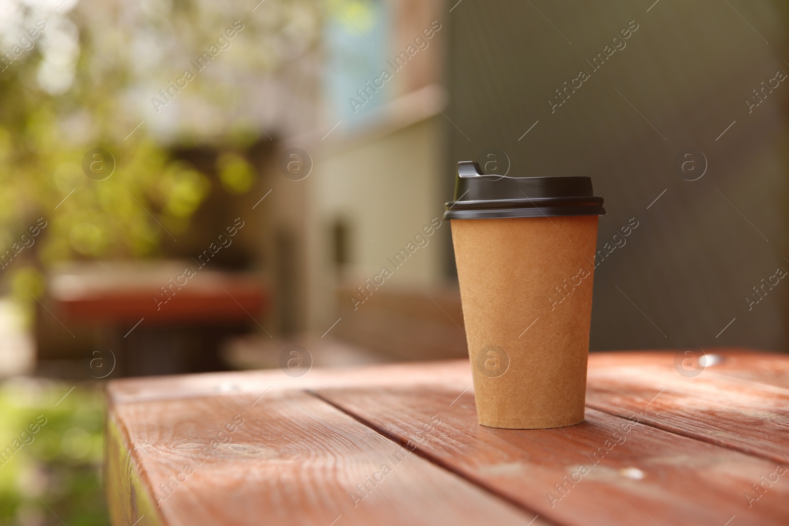 Photo of Takeaway paper coffee cup on wooden table outdoors, space for text