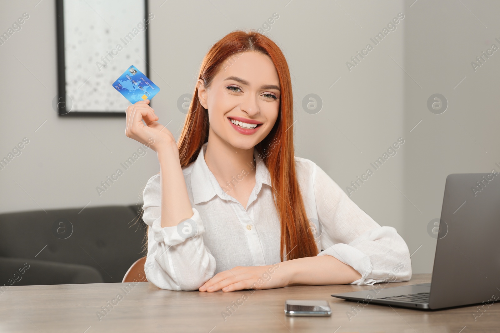 Photo of Happy woman with credit card near laptop at wooden table in room. Online shopping