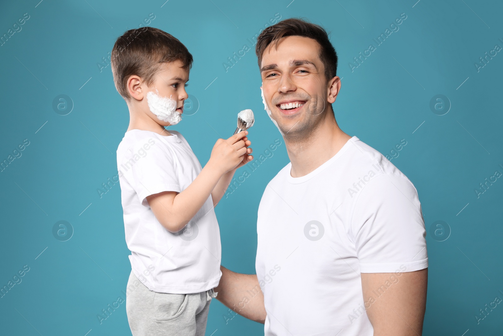 Photo of Son applying shaving foam onto dad's face against color background