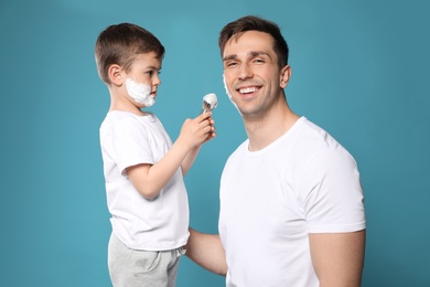 Son applying shaving foam onto dad's face against color background