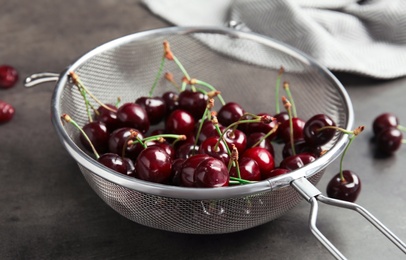 Photo of Sieve with sweet red cherries on table