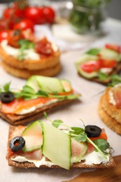 Photo of Tasty rye crispbreads with salmon, cream cheese and vegetables on wooden board. closeup