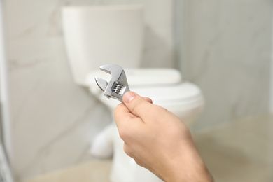 Professional plumber holding wrench near toilet bowl in bathroom, closeup