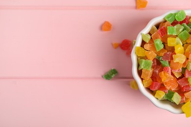 Mix of delicious candied fruits in bowl on pink wooden table, top view. Space for text