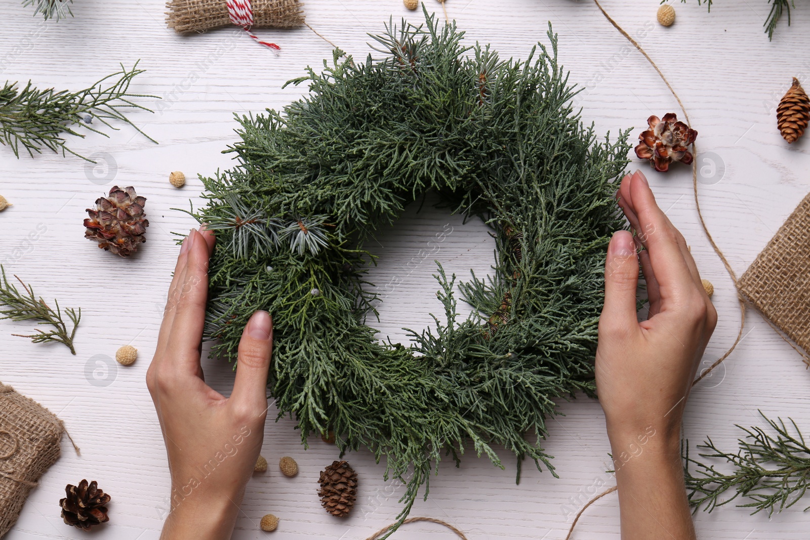 Photo of Florist with beautiful Christmas wreath of fir branches at white wooden table, top view