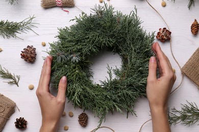 Photo of Florist with beautiful Christmas wreath of fir branches at white wooden table, top view