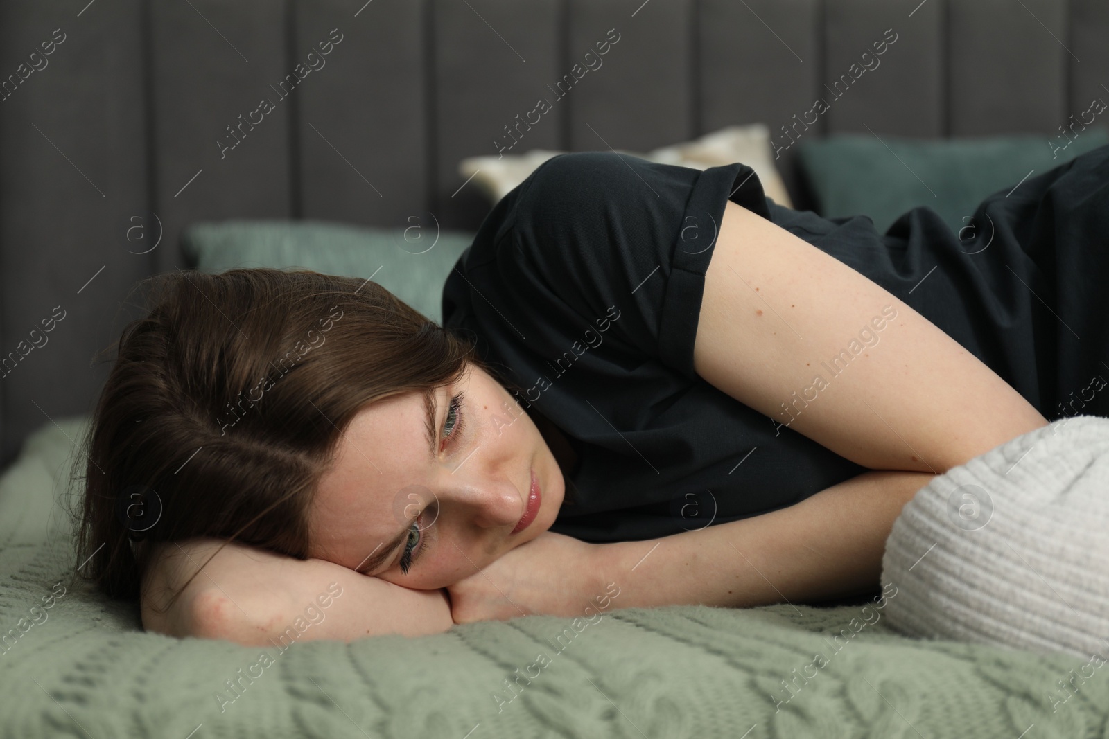 Photo of Sad young woman lying on bed at home