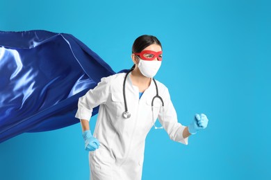 Doctor dressed as superhero posing on light blue background. Concept of medical workers fighting with COVID-19