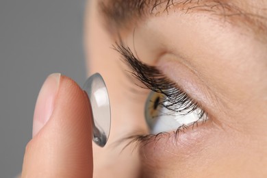 Woman putting in contact lens on grey background, closeup view