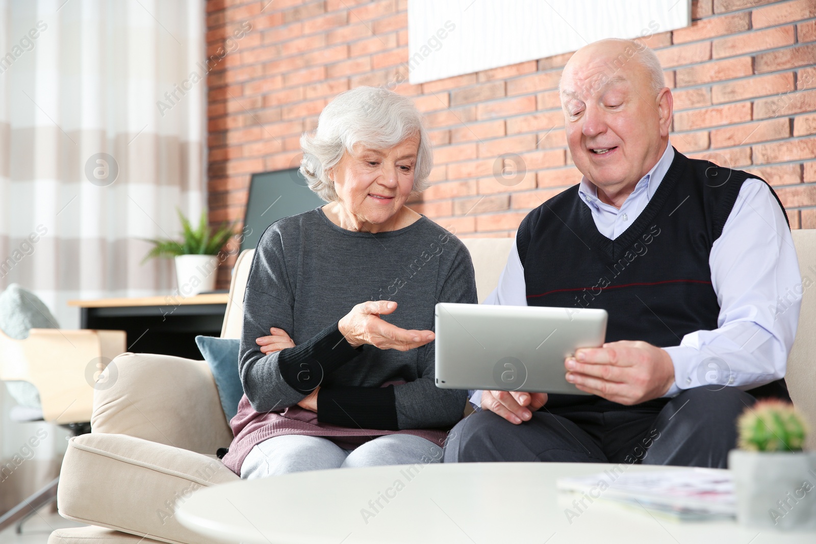 Photo of Elderly couple using tablet PC on sofa in living room