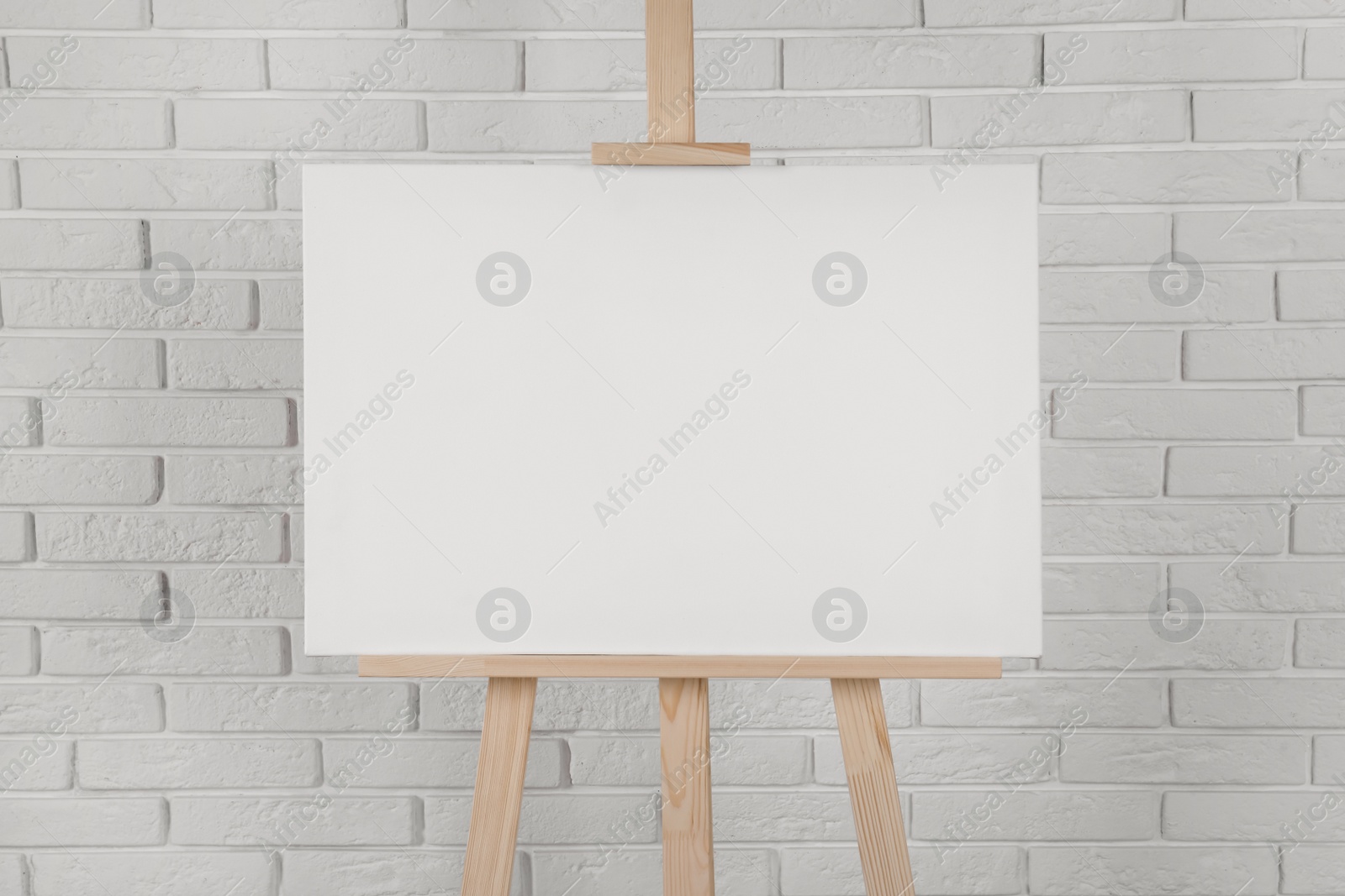 Photo of Wooden easel with blank canvas near white brick wall