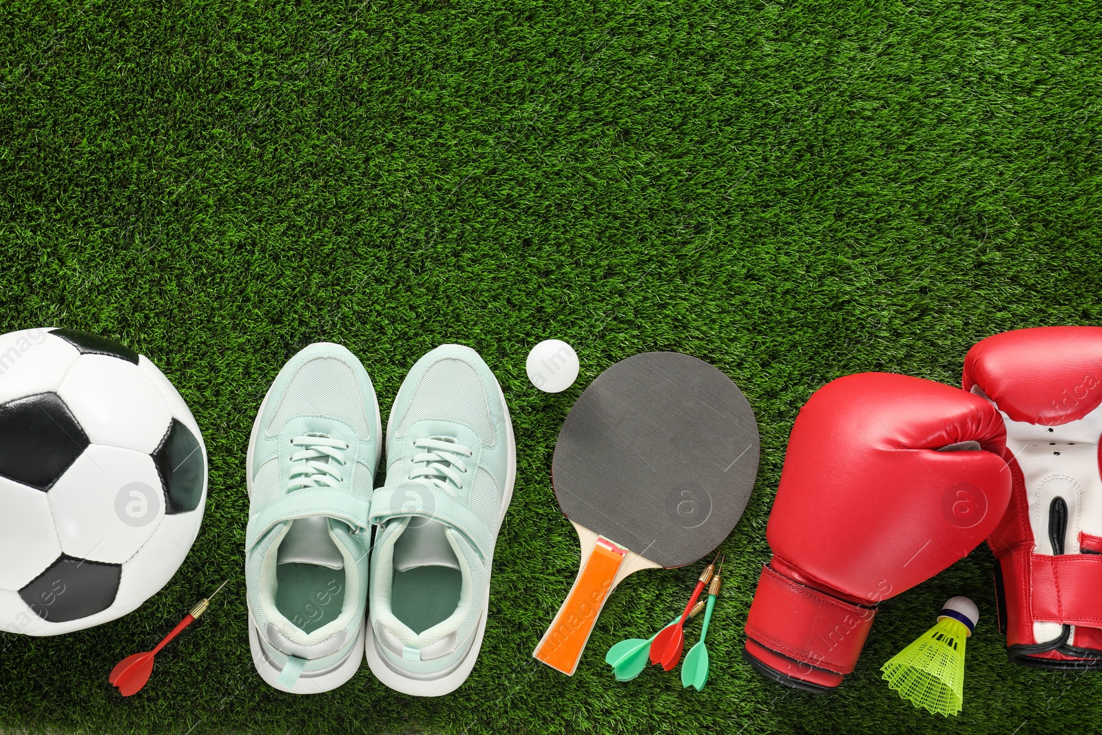 Photo of Different sport equipment and sneakers on green grass, flat lay. Space for text