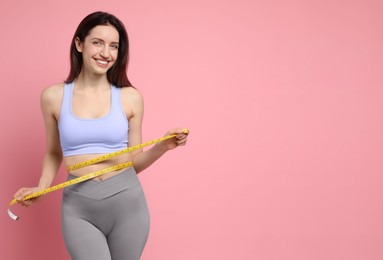 Photo of Happy young woman with measuring tape showing her slim body on pink background, space for text