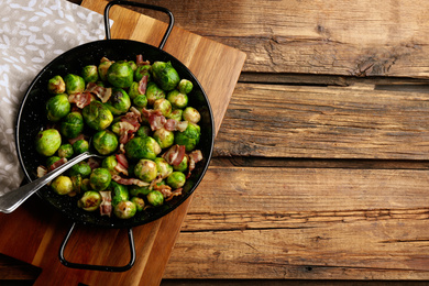 Photo of Delicious Brussels sprouts with bacon on wooden table, flat lay. Space for text