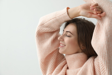Photo of Beautiful young woman wearing warm pink sweater on light background