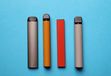 Different electronic cigarettes on light blue background, flat lay
