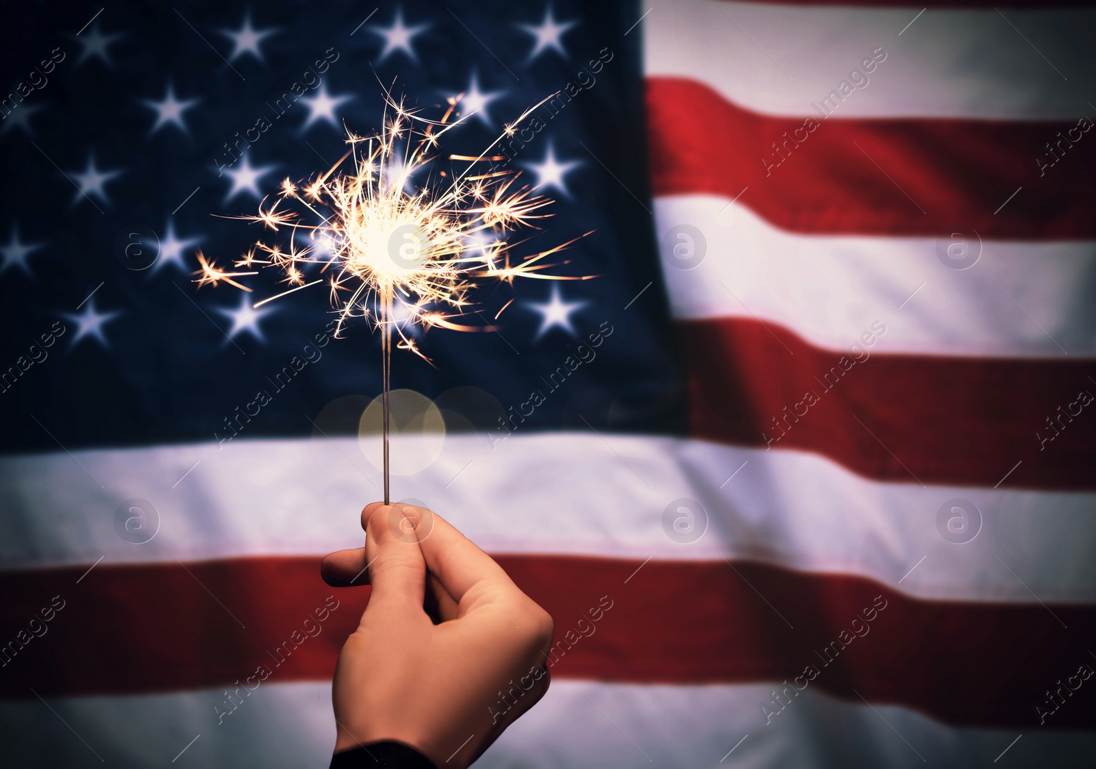 Image of 4th of July - Independence Day of USA. Woman holding burning sparkler against American flag, closeup