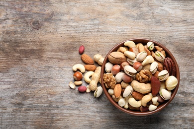 Bowl with mixed organic nuts on wooden background, top view. Space for text