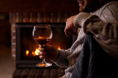 Man with glass of wine near fireplace at home, closeup