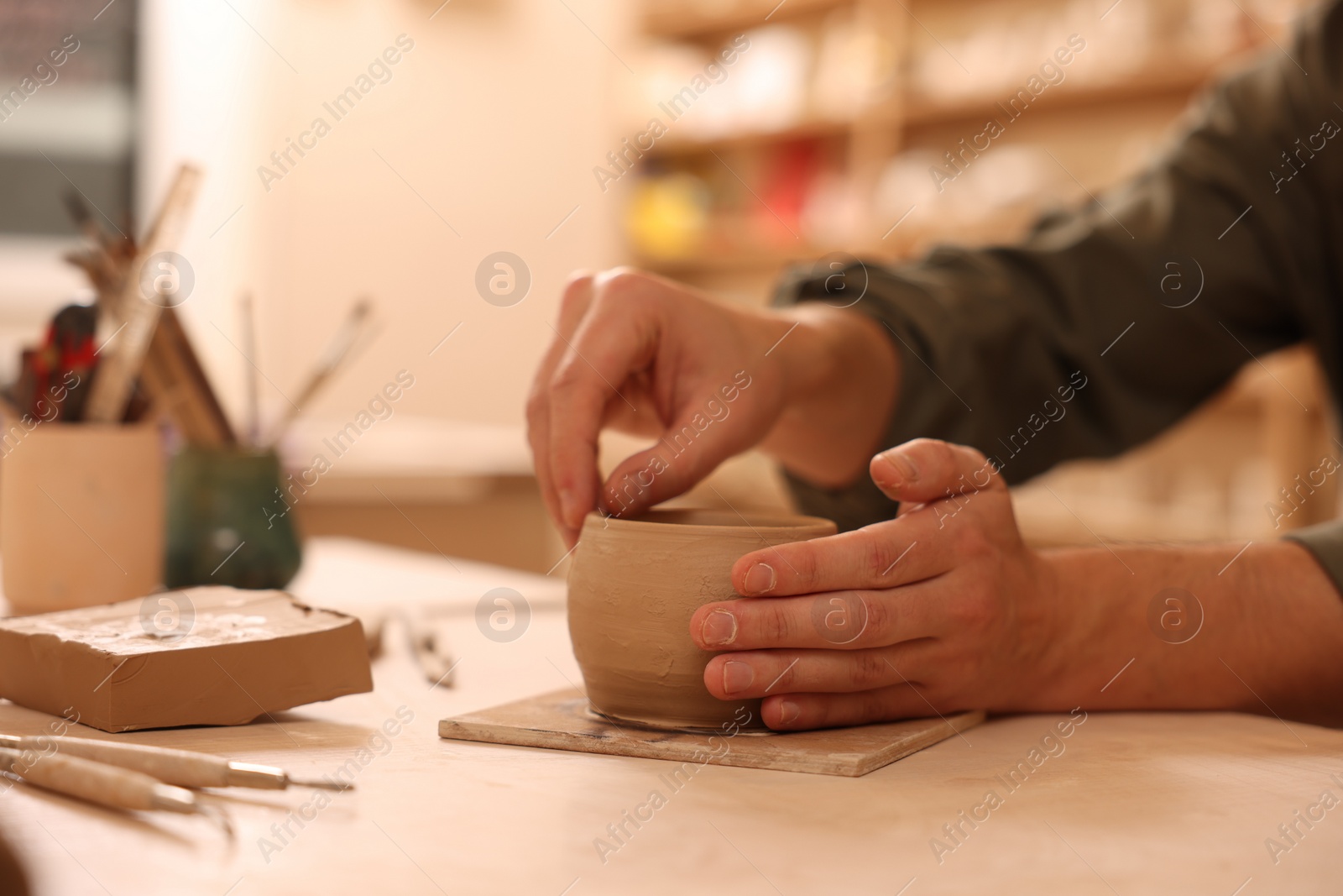 Photo of Clay crafting. Man making bowl at table indoors, closeup