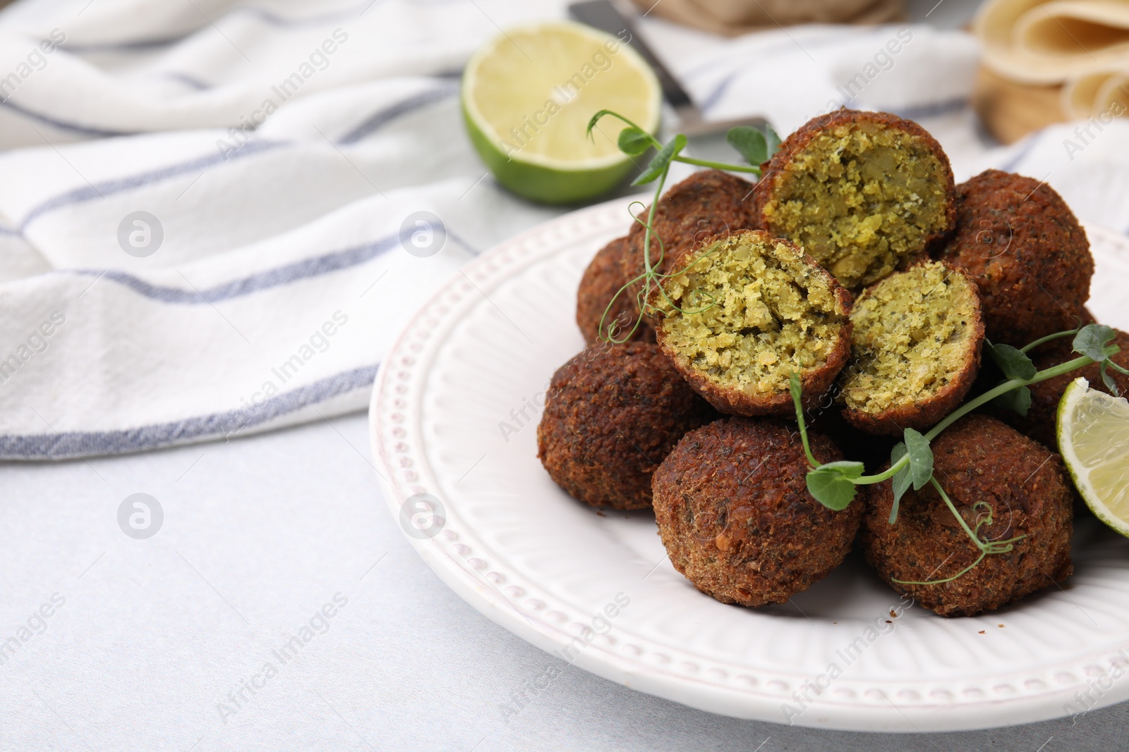 Photo of Delicious falafel balls, lime and microgreens on light table, space for text