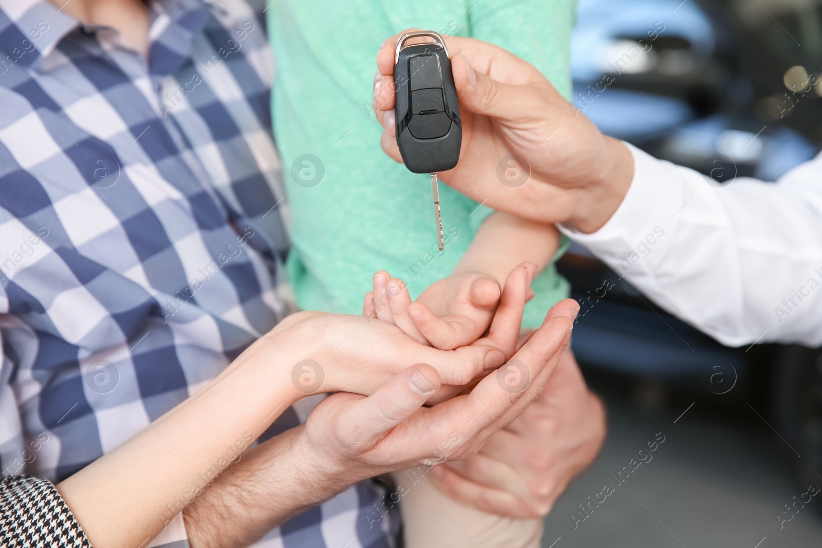 Photo of Salesman giving car key to young family in salon