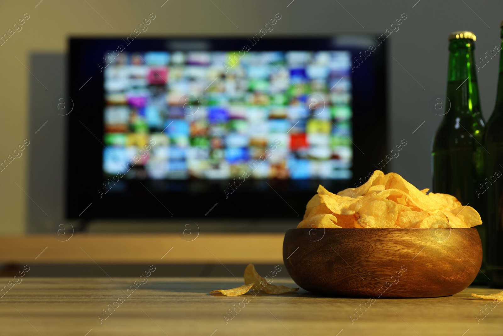 Photo of Modern TV set indoors, focus on table with chips and beer