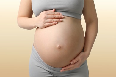 Young pregnant woman touching her belly on beige background, closeup