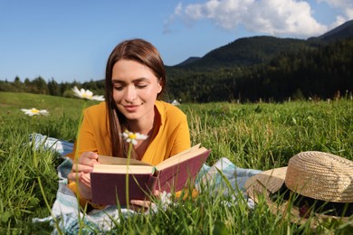 Beautiful young woman reading book on green meadow in mountains
