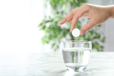 Photo of Woman putting tablet into glass of water indoors, space for text