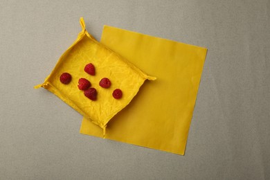 Photo of Orange reusable beeswax food wraps with fresh raspberries on grey background, top view