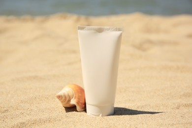 Photo of Sunscreen and seashell on sandy beach. Sun protection care