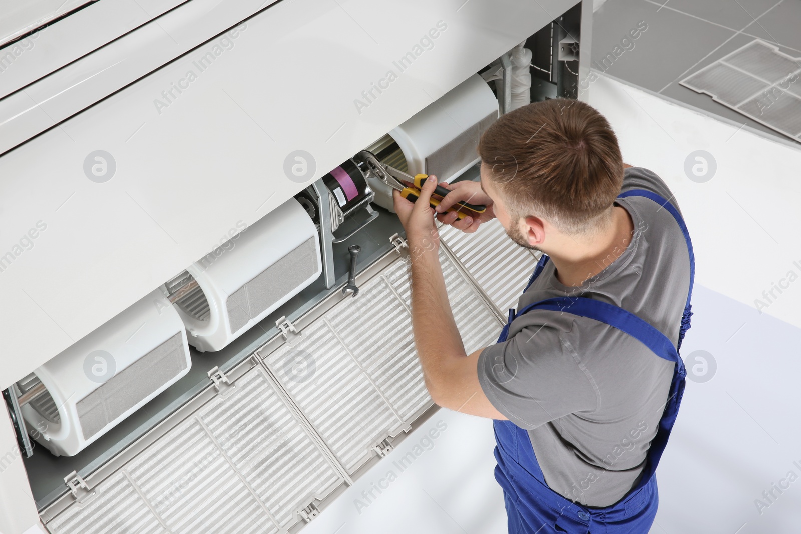 Photo of Young male technician repairing air conditioner indoors