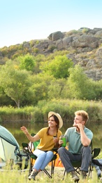 Photo of Young couple with hot drinks resting outdoors. Camping vacation