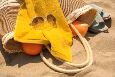 Beach bag, sunglasses and other accessories on sand, closeup