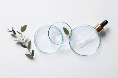 Photo of Petri dishes with samples of cosmetic oil, pipette and green leaves on white background, flat lay