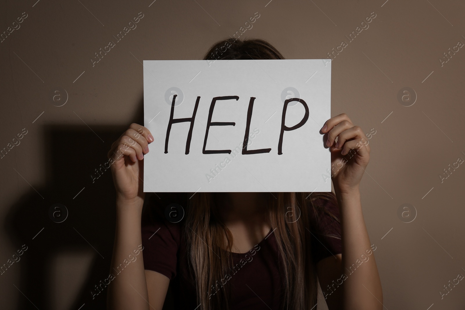 Photo of Young woman with sign HELP near beige wall. Domestic violence concept