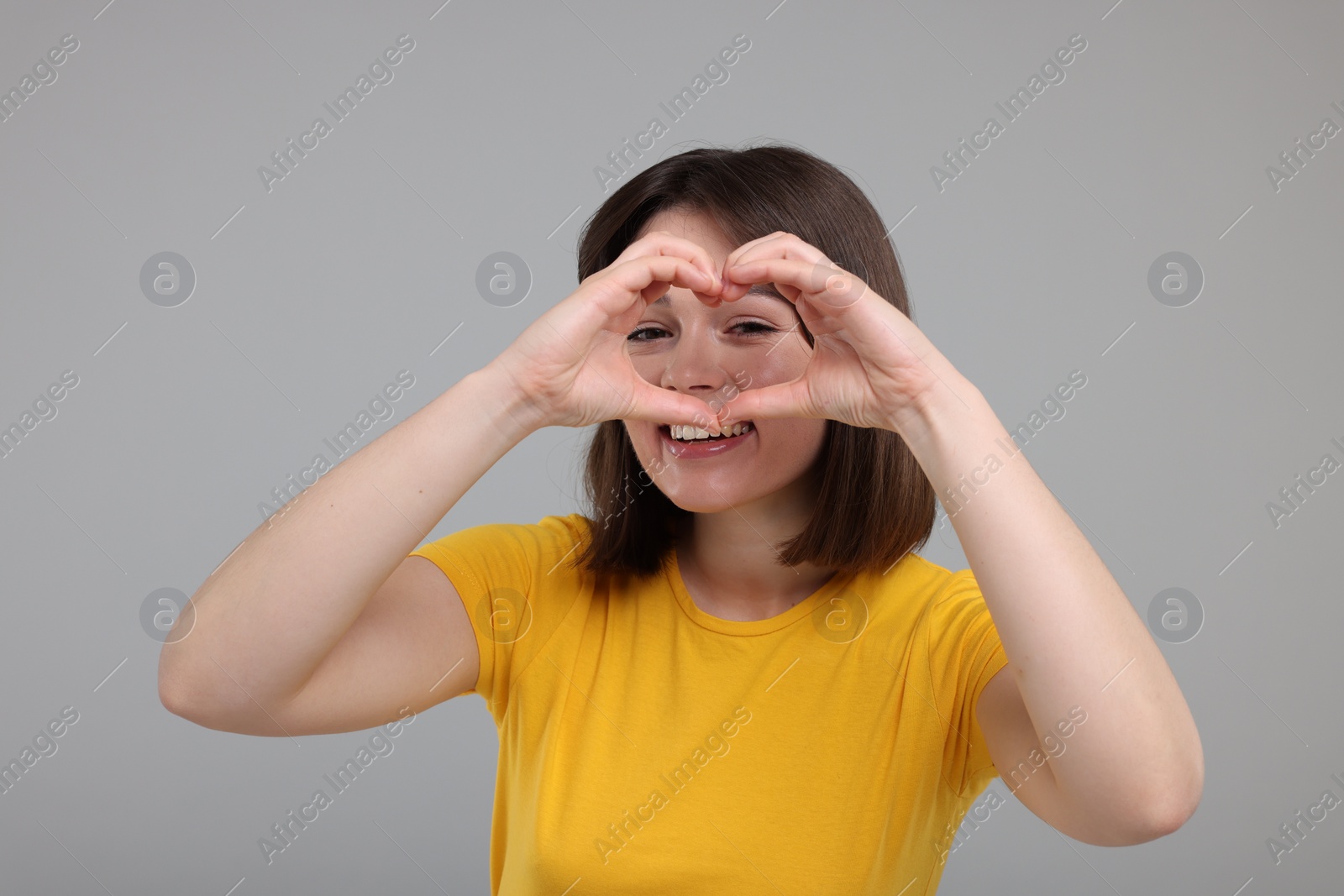 Photo of Happy woman looking through folded in shape of heart hands on grey background