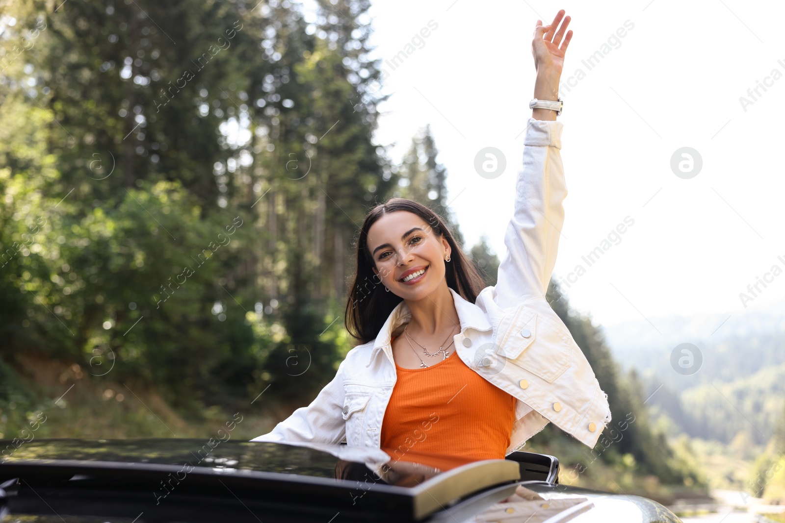 Photo of Enjoying trip. Happy woman leaning out of car roof outdoors