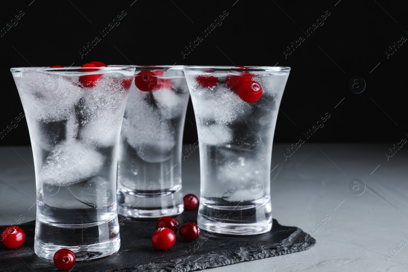 Photo of Vodka in shot glasses and cranberries on grey table