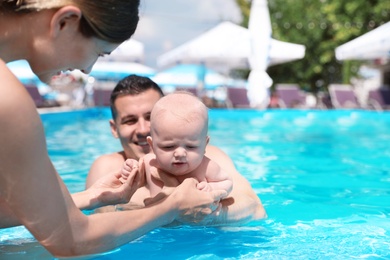 Photo of Happy parents with little baby in swimming pool on sunny day, outdoors