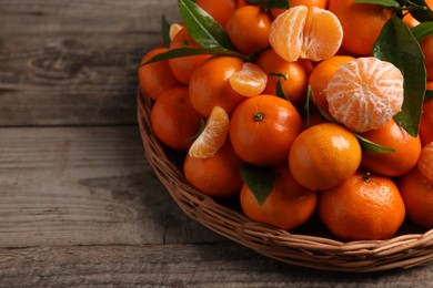 Photo of Fresh ripe juicy tangerines and green leaves on wooden table, space for text