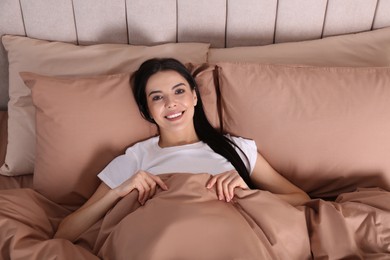 Photo of Woman lying in comfortable bed with beige linens, above view