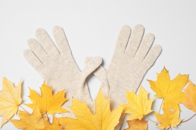 Photo of Stylish woolen gloves and dry leaves on white background, top view