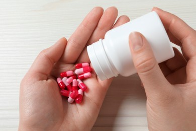 Woman pouring pills from bottle onto hand at white wooden table, closeup