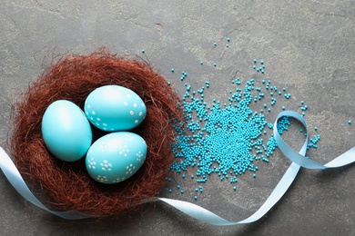 Photo of Flat lay composition with painted Easter eggs in sisal nest on color background, space for text